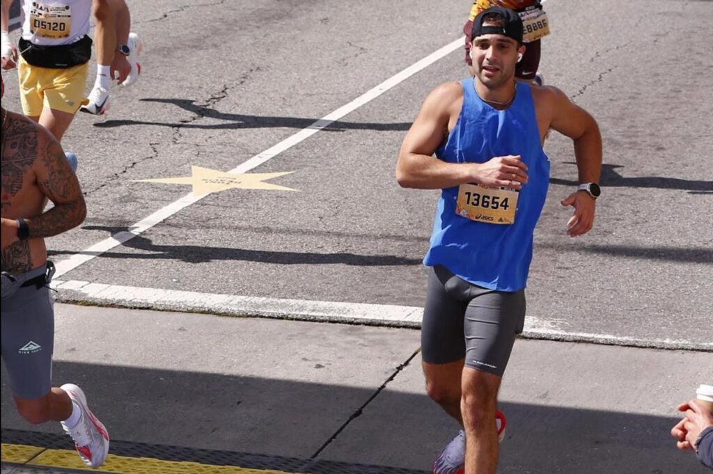 Marathon hydration tips are essential for every runner aiming to improve endurance, boost performance, and recover faster. Marathon runner wearing blue tank top and gray shorts mid-race with race bib 13654